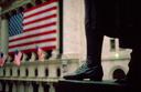 Statue of Washington stands boldly on the steps of the Federal Hall and looking towards the U.S. flag hung on the New York Stock Exchange Building.
